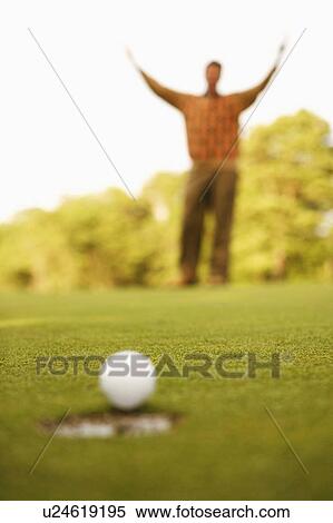 Close-up of a golf ball on the edge of a hole with a man raising his arms in the background View Large Photo Image Stock Photography - Close-up of a golf ball on the edge of a hole with a man raising his arms in the background. Fotosearch