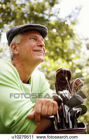Stock Image - Close-up of a mature man leaning on a golf bag and smiling. Fotosearch