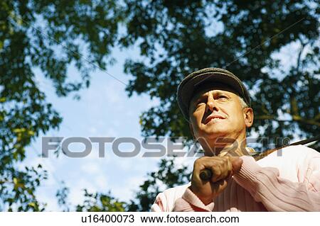 Stock Image - Low angle view of a mature man holding a golf club. Fotosearch