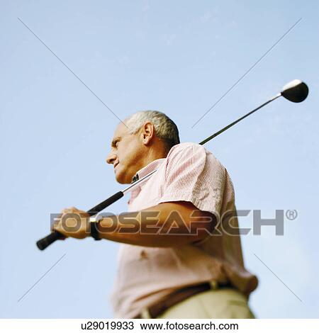 Low angle view of a mature man holding a golf club View Large Photo Image Stock Image - Low angle view of a mature man holding a golf club. Fotosearch