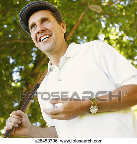 Stock Photograph - Low angle view of a mature man holding a golf club and a golf ball. Fotosearch