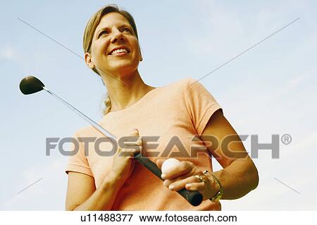 Stock Photo - Low angle view of a mature woman holding a golf club and a golf ball. Fotosearch