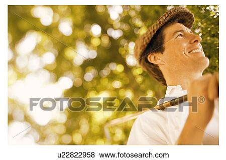 Stock Photo - Low angle view of a mid adult man holding a golf club and smiling. Fotosearch
