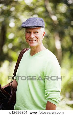 Stock Image - Portrait of a mature man carrying a golf bag and smiling. Fotosearch