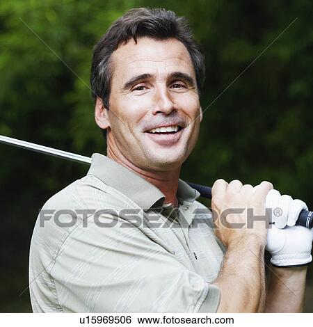Stock Photograph - Portrait of a mature man holding a golf club and smiling. Fotosearch