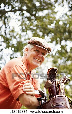 Picture - Portrait of a mature man leaning on a golf bag and smiling. Fotosearch