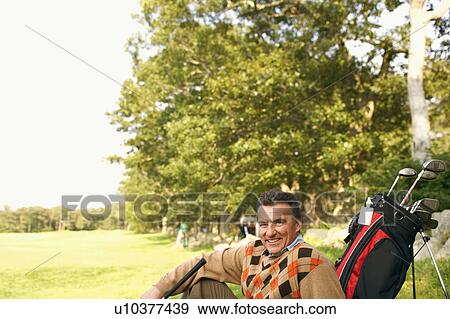 Portrait of a mature man sitting with a golf bag on a golf course View Large Photo Image Stock Photo - Portrait of a mature man sitting with a golf bag on a golf course. Fotosearch