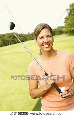 Stock Photograph - Portrait of a mature woman holding a golf club and a golf ball. Fotosearch