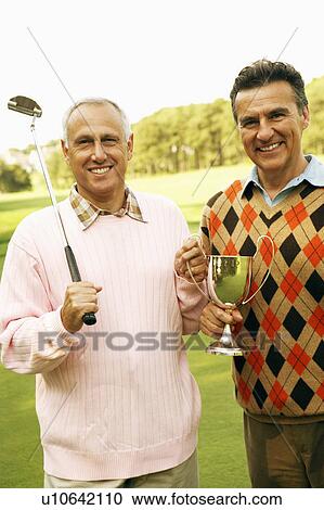 Stock Image - Portrait of two mature men holding a trophy and golf clubs. Fotosearch