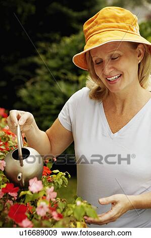 Stock Photo - Close-up of a mature woman watering plants and smiling. Fotosearch