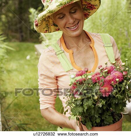 Stock Image - Close-up of a senior woman watering a potted plant and smiling. Fotosearch