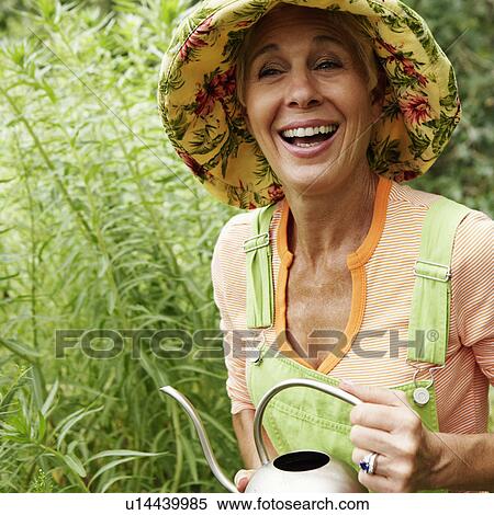 Stock Photography - Close-up of a senior woman watering plants and laughing. Fotosearch