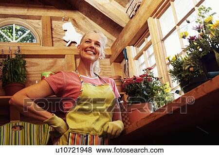 Stock Photo - Low angle view of a mature woman standing near potted plants. Fotosearch