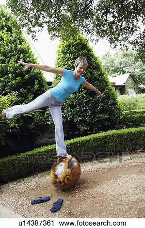 Stock Image - Mature woman standing on one leg on a rock. Fotosearch