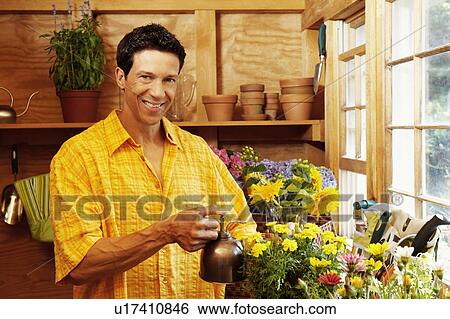 Stock Photograph - Portrait of a mature man spraying water over potted plants. Fotosearch