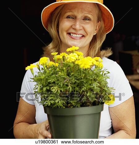 Stock Image - Portrait of a mature woman holding a potted plant and smiling. Fotosearch