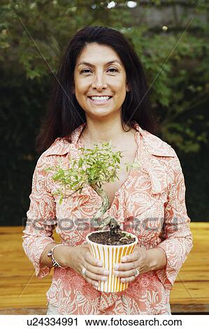 Stock Image - Portrait of a mature woman holding a potted plant and smiling. Fotosearch