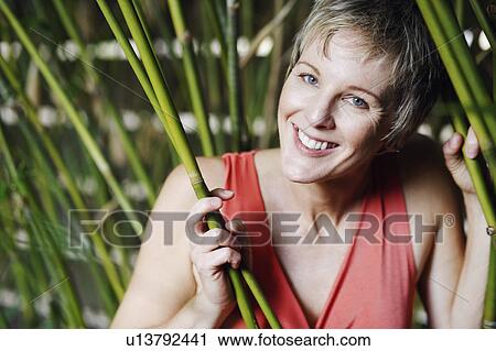 Stock Image - Portrait of a mature woman holding bamboo plants and smiling. Fotosearch
