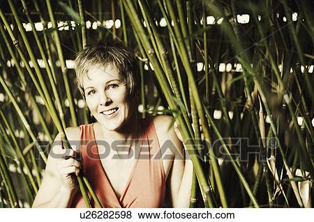 Stock Photo - Portrait of a mature woman holding bamboo plants and smiling. Fotosearch