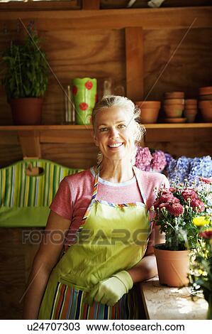 Stock Image - Portrait of a mature woman standing near potted plants. Fotosearch