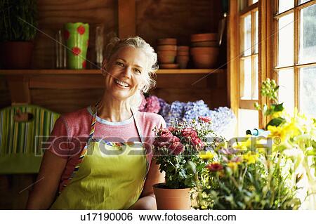 Stock Photograph - Portrait of a mature woman standing near potted plants. Fotosearch