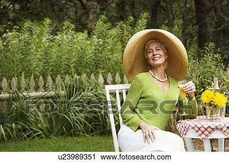 Stock Image - Portrait of a senior woman sitting on a chair holding a glass of juice. Fotosearch