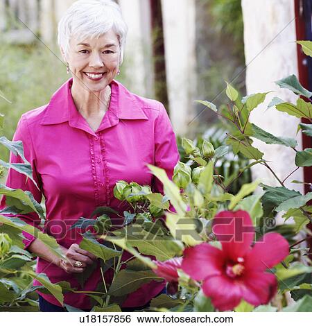 Stock Photograph - Portrait of a senior woman standing behind plants. Fotosearch