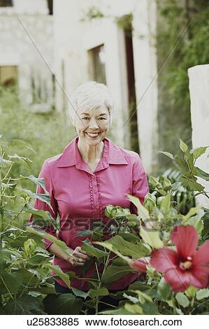 Stock Photography - Portrait of a senior woman standing behind plants. Fotosearch