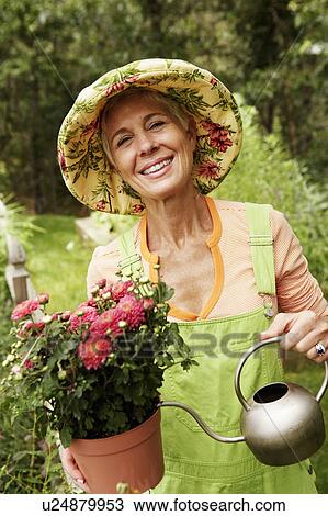 Stock Image - Portrait of a senior woman watering in a potted plant and smiling. Fotosearch
