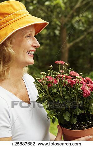 Stock Image - Side profile of a mature woman holding a potted plant and smiling. Fotosearch
