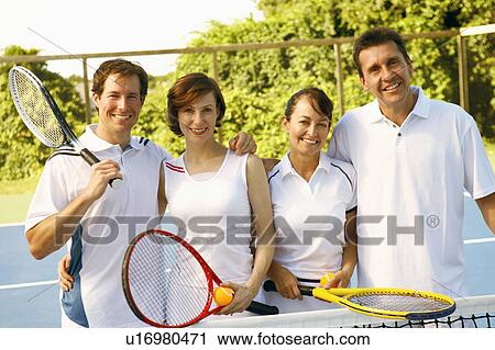 Stock Image - Portrait of a mid adult couple and a mature couple standing together on a tennis court. Fotosearch