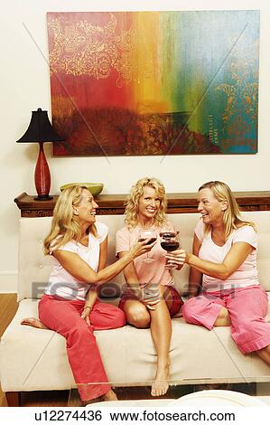 Stock Photograph - Portrait of a mid adult woman sitting with her two friends toasting glasses of wine. Fotosearch