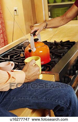 Stock Photo - Close-up of a woman's hand holding a kettle with a man's hand holding a cup of tea. Fotosearch