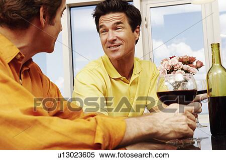 Stock Photography - Close-up of two mature men holding glasses of wine and talking. Fotosearch