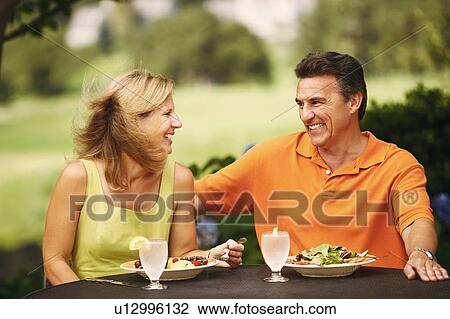 Stock Image - Mature couple sitting at the table with plates of salad in front of them. Fotosearch