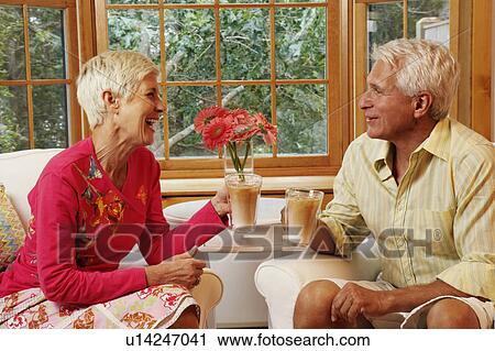 Stock Image - mature man and a senior woman sitting on chairs and holding mugs of coffee. Fotosearch