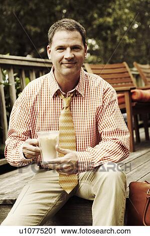 Stock Image - Portrait of a businessman holding a mug of milkshake and smiling. Fotosearch