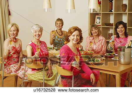 Stock Photo - Portrait of a group of mature women sitting at the dining table and holding champagne flutes. Fotosearch