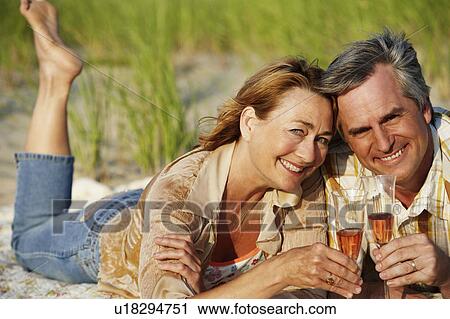 Portrait of a mature couple lying on the beach and holding champagne flutes View Large Photo Image Stock Image - Portrait of a mature couple lying on the beach and holding champagne flutes. Fotosearch