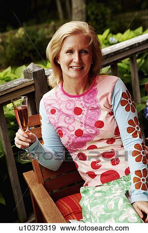 Stock Photo - Portrait of a mature woman holding a champagne flute and smiling. Fotosearch