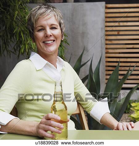Portrait of a mature woman holding a bottle of wine and smiling View Large Photo Image Stock Photo - Portrait of a mature woman holding a bottle of wine and smiling. Fotosearch