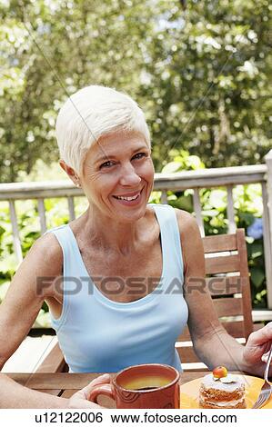 Portrait of a mature woman sitting at the table with a plate of dessert in front of her and smiling View Large Photo Image Stock Photograph - Portrait of a mature woman sitting at the table with a plate of dessert in front of her and smiling. Fotosearch