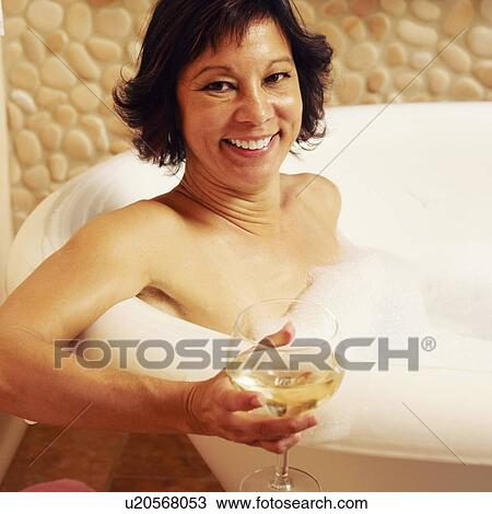 Stock Image - Portrait of a mature woman sitting in a bathtub and holding a glass of wine. Fotosearch