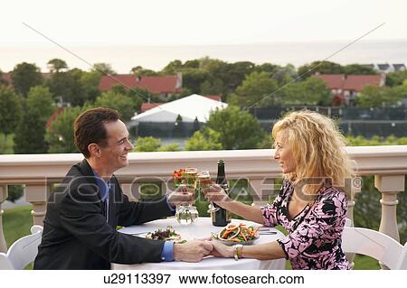 Side profile of a mature couple sitting at the table and toasting with champagne flutes View Large Photo Image Stock Photo - Side profile of a mature couple sitting at the table and toasting with champagne flutes. Fotosearch