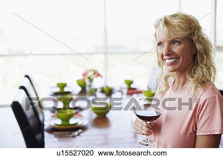 Stock Image - Side profile of a mid adult woman holding a glass of wine and smiling. Fotosearch