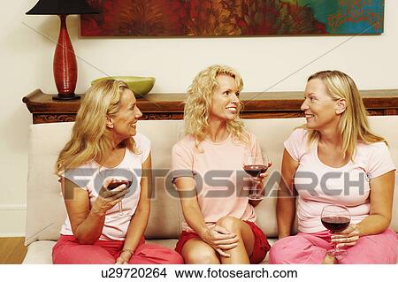 Three women sitting together and holding glasses of wine View Large Photo Image Picture - Three women sitting together and holding glasses of wine. Fotosearch