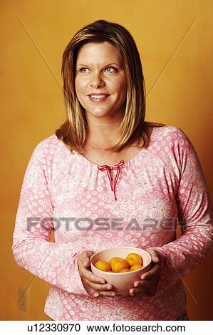 Stock Image - Close-up of a mature woman holding a bowl of peaches and looking away. Fotosearch