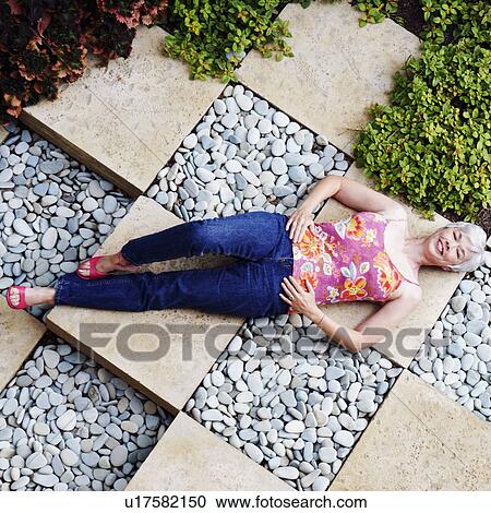 Stock Image - High angle view of a senior woman lying in a garden. Fotosearch