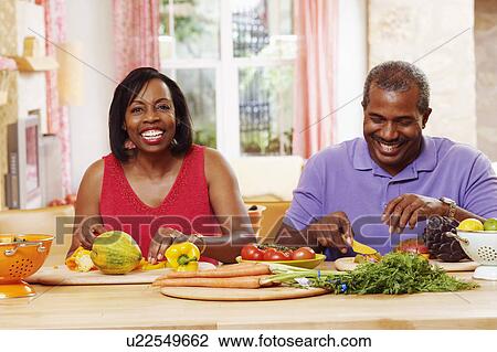 Stock Image - Portrait of a mature couple cutting vegetables and smiling. Fotosearch