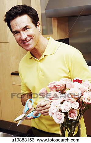 Stock Image - Portrait of a mature man cutting the stems of roses and smiling. Fotosearch